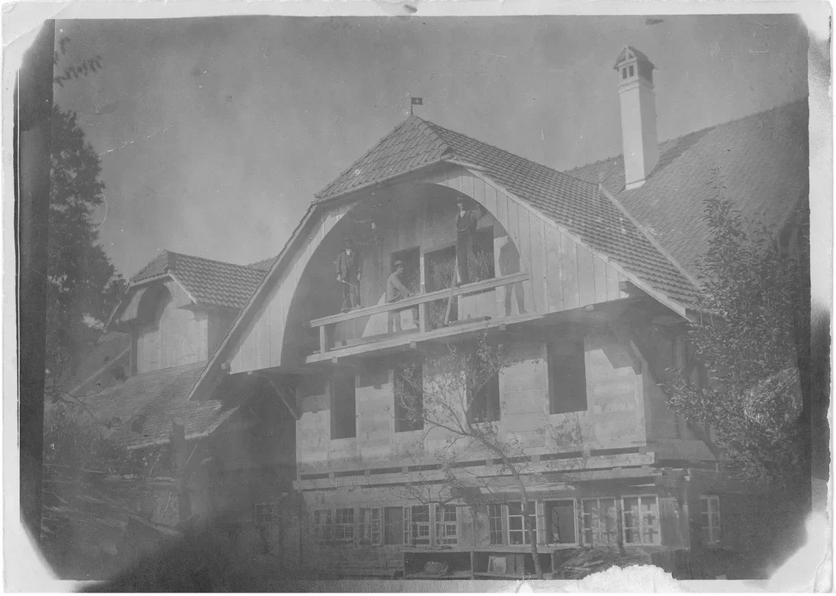 Altes Schwarzweissfoto: drei Männer auf dem Balkon unter dem Giebel des Bauernhauses im Bau