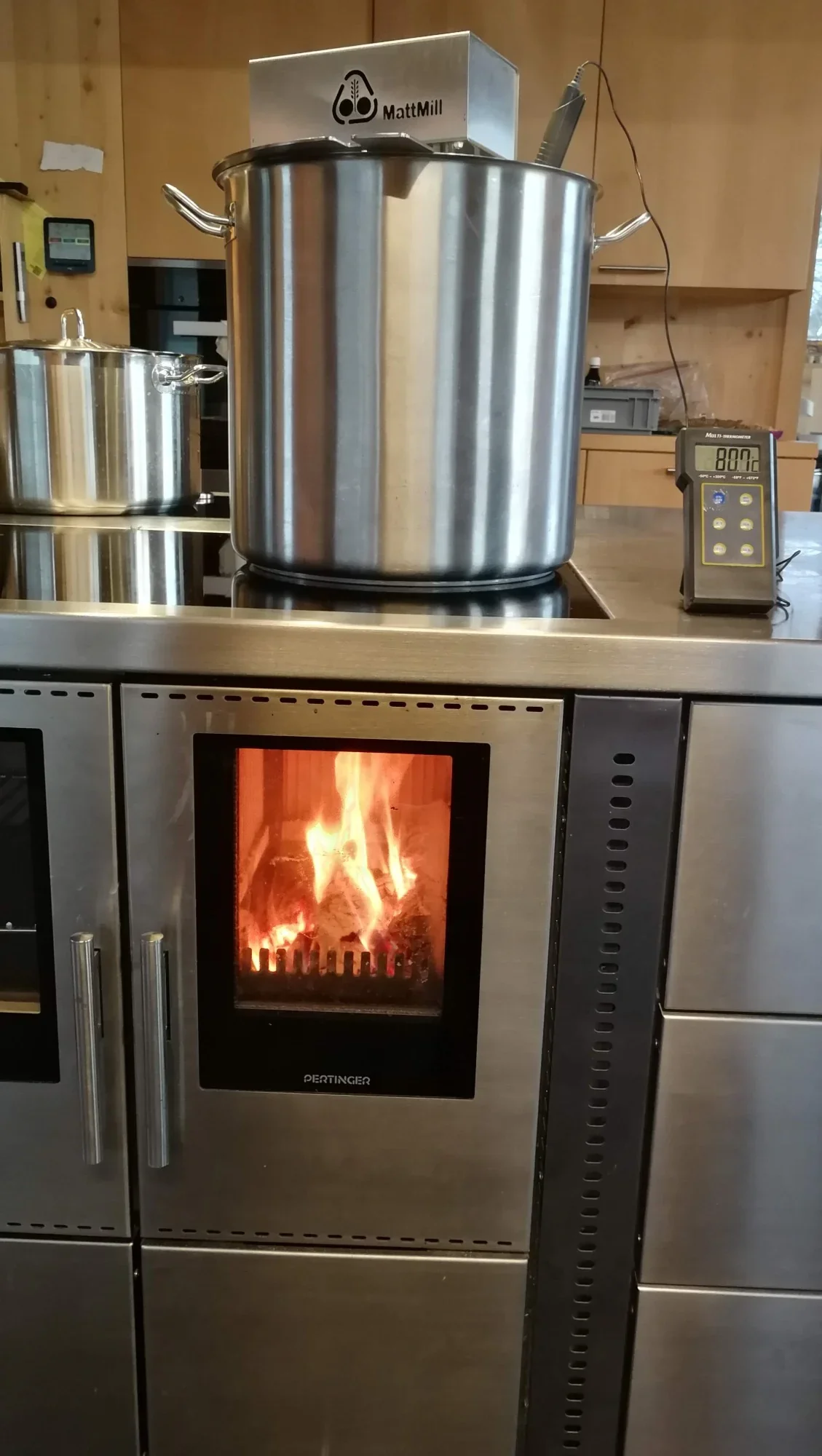 Grosser Edelstahltopf mit Rührwerk auf dem Küchenherd, daneben ein Thermometer